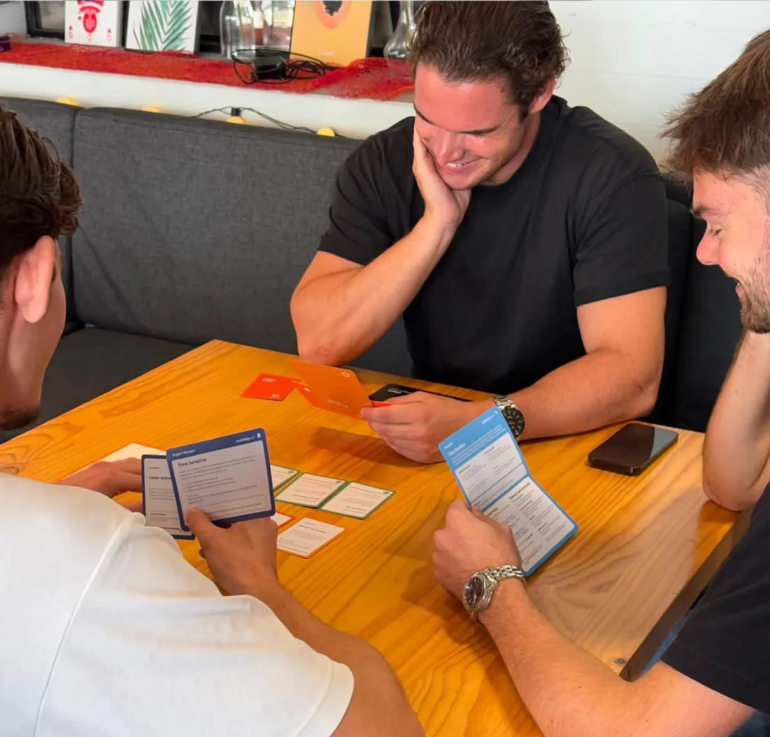 Three players around a table with Client Quest cards in hand, one of them laughing