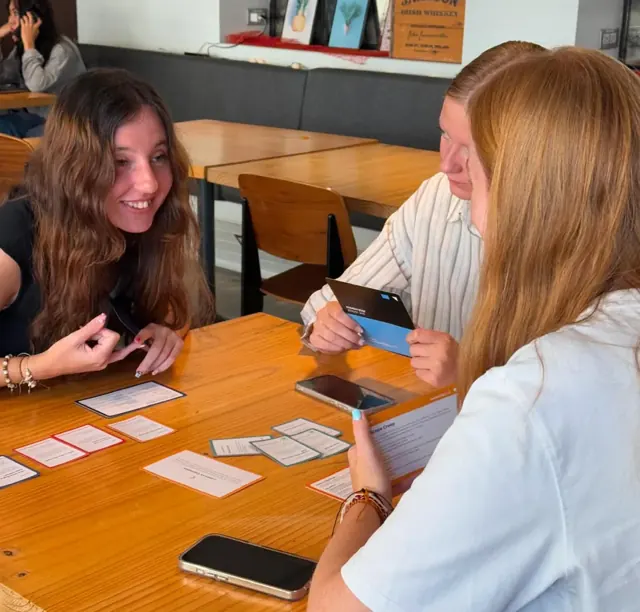 Three players at a table, mid-round, laughing over their cards